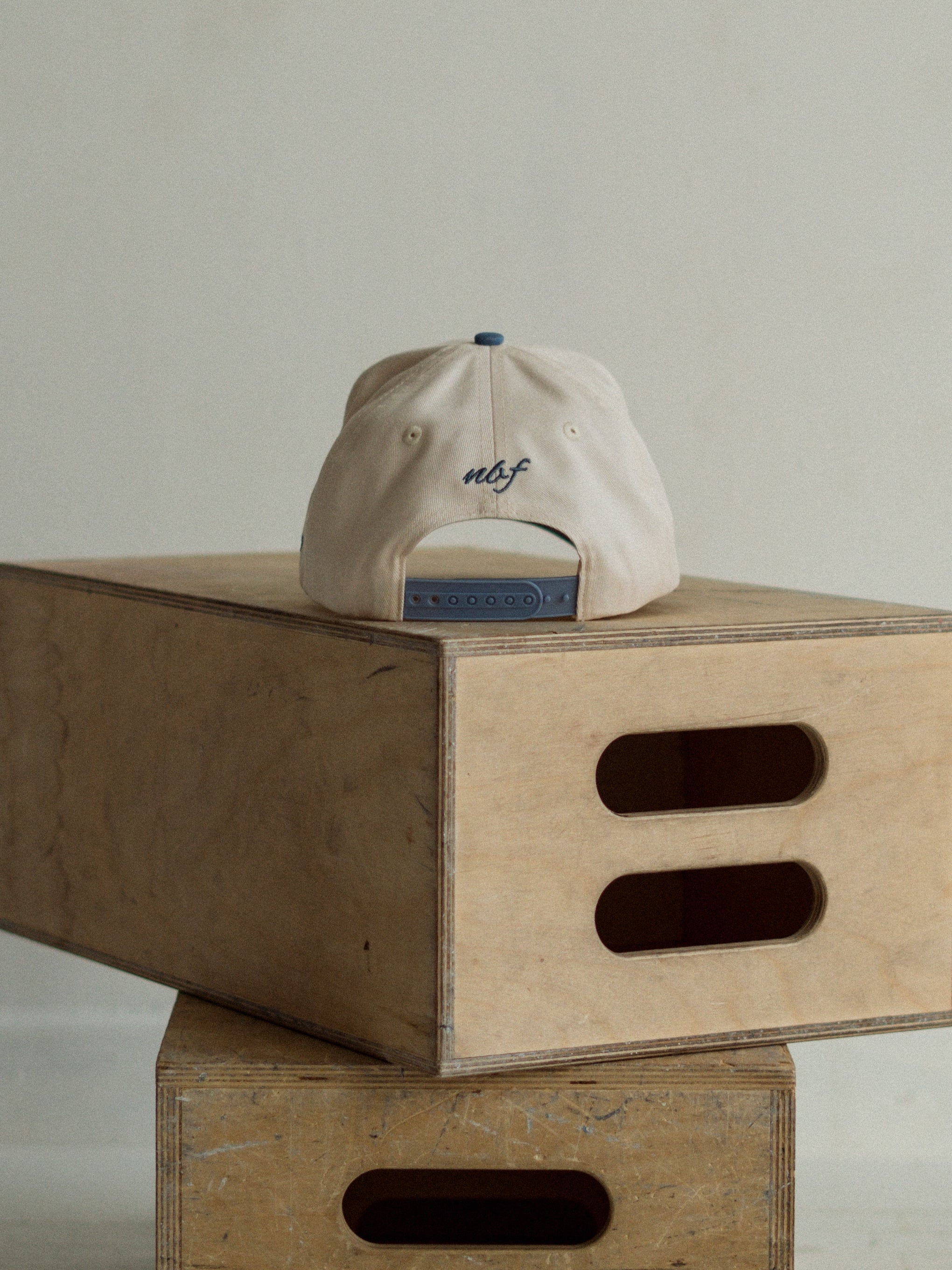 Beige cap with blue brim on a wooden box against a plain background